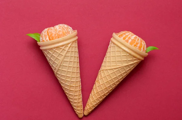two waffle cones with ripe tangerines on a red background close up