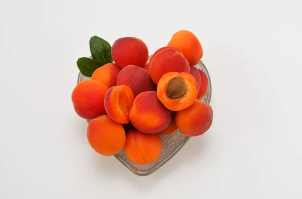 Beyaz arka planda, kalp şeklinde bir kasede olgun kayısılar yatıyordu.