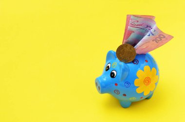 Sarı arka planda mavi bir kumbara ve bir hryvnia ve iki yüz hryvnia sikke, kopyala uzay