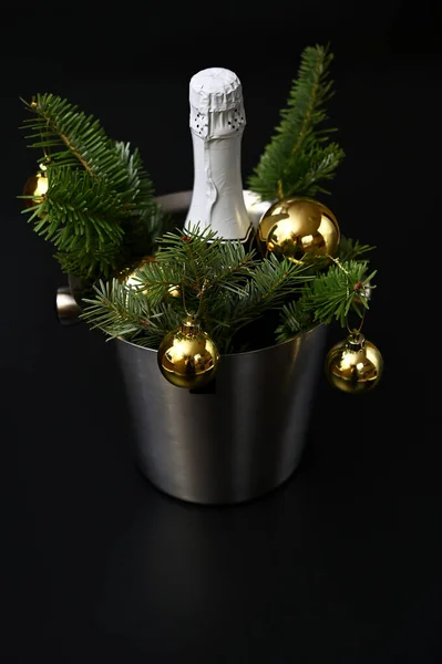 New Year\'s decor, a bottle of champagne, fir branches and golden balls on a dark background