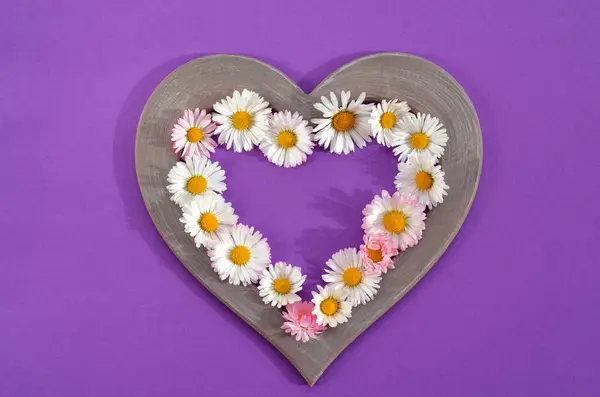 heart shaped frame with whole flowers on a purple background close up