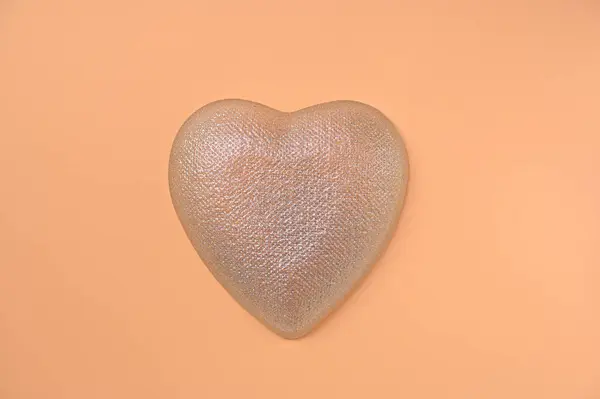 silver heart on a peach background close up