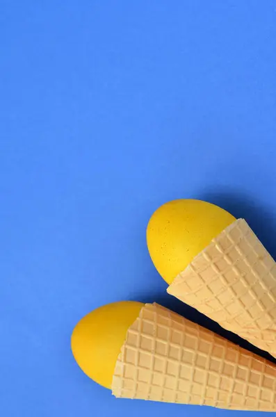 yellow Easter eggs in waffle cones on a blue background, copy space