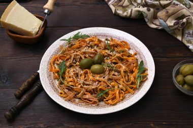 Ahşap bir masa üzerinde renkli makarna, peynir, zeytin ve otlarla dolu bir tabak.