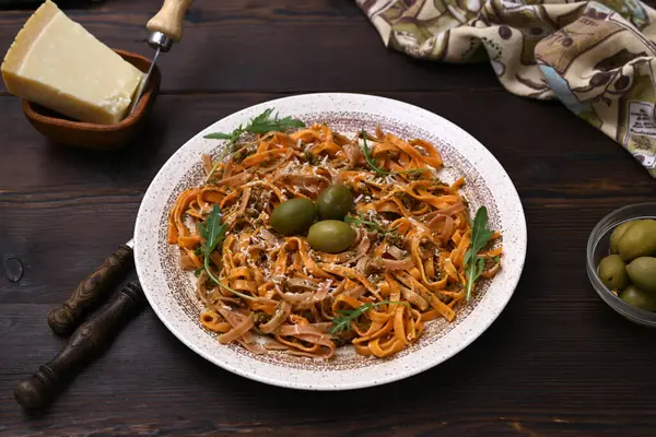 Ahşap bir masa üzerinde renkli makarna, peynir, zeytin ve otlarla dolu bir tabak.