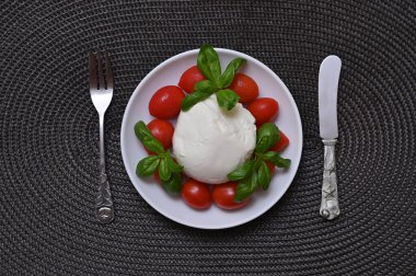 mozzarella peyniri, domates ve taze fesleğen bir tabakta koyu bir arka planda yatıyordu.