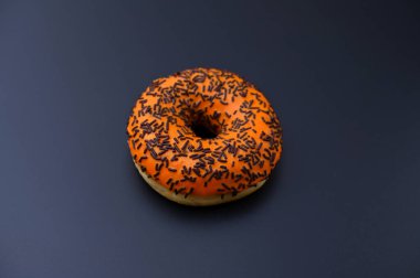 Siyah arka planda çikolata parçacıkları olan turuncu jöleli donut.