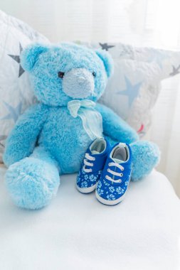 Oyuncak mavi ayılı bir çocuk yatağı ve yakınlarda küçük ayakkabılar, çocukların odasının içi. Çocuk aksesuarları.