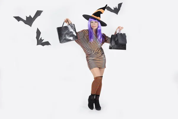 戴着一顶紫色头发的女巫帽 穿着鲜艳衣服的女人 带着采购的纸袋 与白色隔离 万圣节的假日折扣 黑色星期五 销售概念 假日购物 — 图库照片