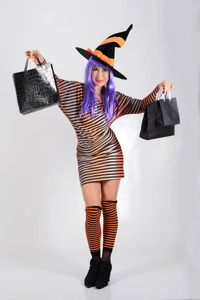 戴着一顶紫色头发的女巫帽 穿着鲜艳衣服的女人 带着采购的纸袋 与白色隔离 万圣节的假日折扣 黑色星期五 销售概念 假日购物 — 图库照片