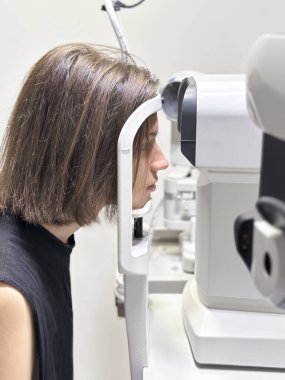 Genç bir adam gözlükçüde modern dijital bir bilgisayar görme test makinesinde oturuyor, seçici odaklanma, yakın çekim.