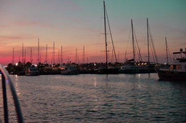 Akdeniz 'in sularındaki limandaki yatların gölgelerinin güzel manzarası gün batımının arka ışığında mor, turuncu, gökyüzü ve gece kıyılarının ışıklarına karşı..