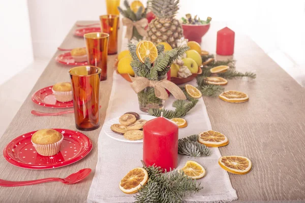 Christmas holiday table decorated with candles, Christmas tree branches, dried oranges, sweets and fruits,selective focus.Cozy house decorated for the holiday with handmade items.Christmas decoration.