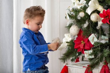 Çocuk, Noel ağacını oynuyor ve süslüyor, yakın plan, yarım vücut. Küçük çocuk, Noel oyuncaklarını evin içindeki bir Noel ağacına asıyor..