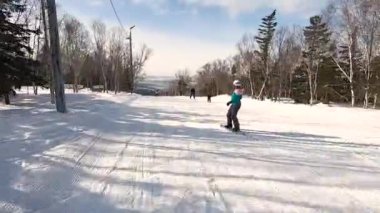 Spor gözlüklü snowboardcu ve özel bir takım elbiseli kar kaplı bir dağdan kayarak kayıyor, bir tahtada manevra yapıyor.