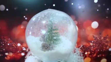 İçinde karlı, köknar ağacı ve çam kozalakları olan şeffaf bir top bulanık ışıkların neşeli arka planında dönüyor. Yılbaşı dekorasyonu ve bir hatıra. Süslü Noel mağazası penceresi