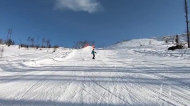 Spor gözlüklü snowboardcu ve özel bir takım elbiseli kar kaplı bir dağdan kayarak kayıyor, bir tahtada manevra yapıyor.