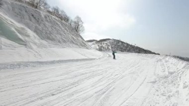 Güzel, karlı bir yamaçta, buzla kaplı bir kamera hareketi ve güneşli bir günde panoda korkan bir snowboardcunun videosu. Kış sporları ve açık hava eğlencesi