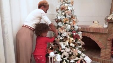 Afrikalı koyu tenli anne ve çocuk Noel topunu süslü bir Noel ağacına şöminenin yanına asıp eğleniyorlar. Noel ağacını aile süslemesi. Noel zamanı.