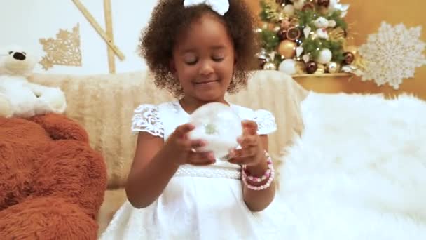 一个穿着雅致衣服 皮肤漆黑的小女孩拿着雪球玩耍 在圣诞节的背景下嬉笑着 圣诞节期间 — 图库视频影像