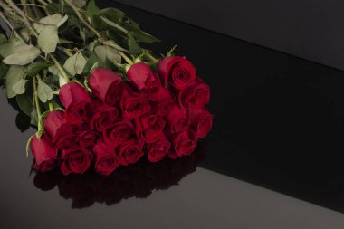 An elegant gift bouquet of long red roses of the Freedom variety with closed buds on a black table and a black background. A symbol of love. Funeral bouquet of red long roses. Background of grief.