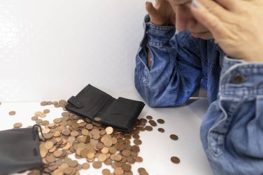 Stres duyguları olan yaşlı bir kadın ellerini cüzdanı ve kumbarası olan küçük paralardan oluşan bir dağın üzerinde tutuyor. Yoksulluk, para krizi, küçük emeklilik kavramı.