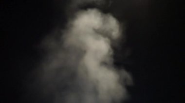 Kara gece gökyüzünün arka planında duman bulutları uçuşuyor.