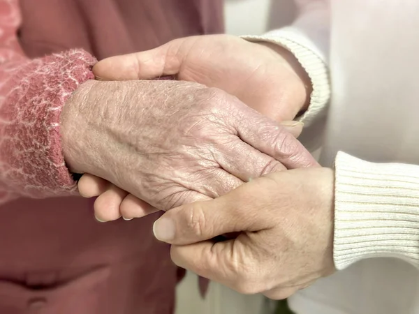 Interweaving of generations: hands of young and old people close-up. Gentle touch of the hands of a young woman and the hands of an elderly woman, symbolizing eternal care and love. Mother\'s Day.