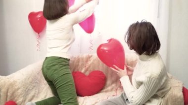 Tatil için hazırlık. Bir çift aşık yatak odasını kalp şeklinde balonlarla süslüyor. Romantik eğlence