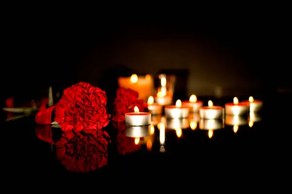 Red carnation flowers and many burning candles in memory of the deceased of the funeral. Sad mourning background