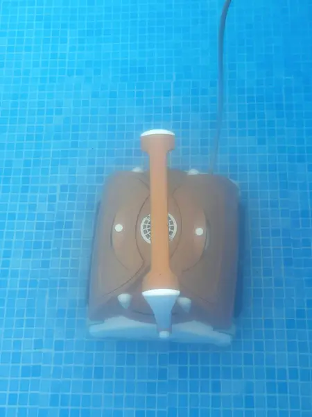 Water robot vacuum cleaner cleans, removes debris on the bottom, walls of the pool, top view through translucent water. Pool cleaning process. Preparing for the summer season. Smart home technologies