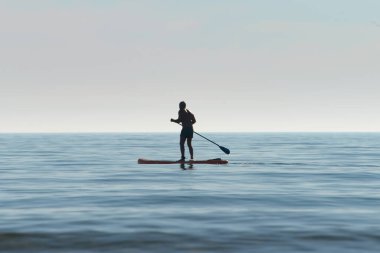 Şahsi bir kanoyla kayıkçı silueti, şafak vakti okyanusun sakin sularında kürek çeken bir kano. Yaz tatili Denizde suyun üzerinde