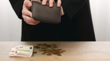 Yavaş çekim videosu. Bir adam cüzdanındaki para ve sentleri akıllı banknotların yanında sallıyor. Masadaki parayı eliyle sayıyor. Fonların hesaplanması ve kontrolü