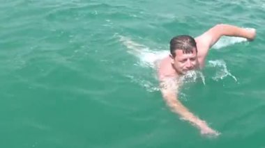 Turquesa renginde tropikal sıcakta orta yaşlı atletik formda bir adam geniş bir yelpazeyle yüzer.