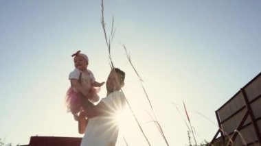 Baba, gülen küçük kızını güneşin batışında, mutlu bir ailenin, ebeveynlerin ve çocukların vakit geçirdiği romantik bir videoyla etrafında döndürür.