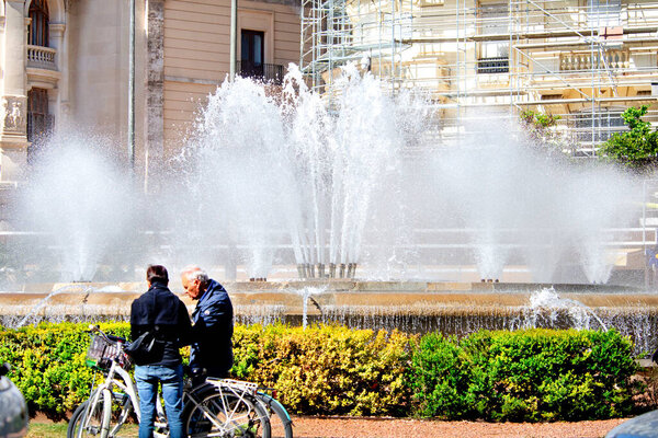 City fountain in a sunny cityscape in the heat with people.Clouds of splashes, drops and jets of a fountain close-up glisten in the sun's rays. The coolness of a summer fountain.  PHOTO CREATED USING A photoCAMERA NIKON 610