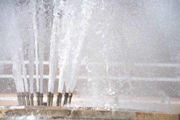 Clouds of splashes, drops and jets of a fountain close-up glisten in the sun's rays. The coolness of a summer fountain