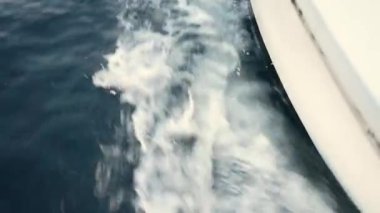 Yatın hareket halindeki deniz suyu sıçramaları ve sıçramaları yatın gövdesinin bir kısmıyla, yakın plan. Gün batımında denizde dalgalar ve su gemisinin hareketi