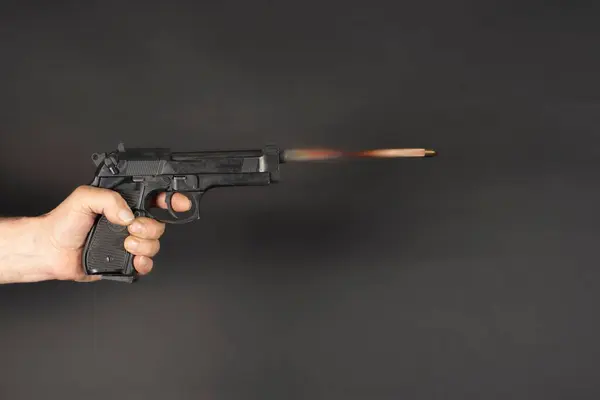 stock image A hand shoots from a black pistol, the bullet flies with a fiery trail on a dark background. Hand with a weapon, bullet trajectory in motion