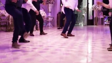 Bir grup adam resmi bir etkinlikte enerjik bir şekilde dans ediyor. Parlak bir zeminde yakın plan çekimde çekiliyor.,