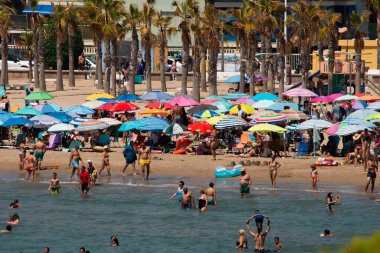Renkli şemsiyeli kalabalık plajlar, yüzen insanlar, palmiye ağaçları, sıcakta turistik oteller. Kalabalık plaj