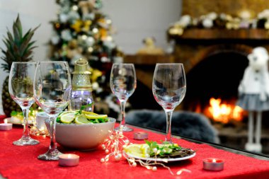 Noel yemeği için şarap kadehleri, mezeler ve şöminenin önündeki Noel süslemeleri ve Noel ağacı.
