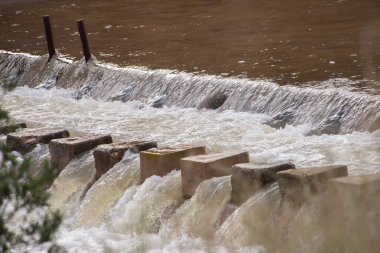 Çamurlu, taşan nehir suyu akıntısı beton yarık yapıları tarafından kırılır. Sel.