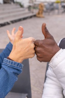 Two hands with white skin and dark skin holding thumbs up close, gesture of unity and cooperation, teamwork, success, friendship of nations and respect. clipart