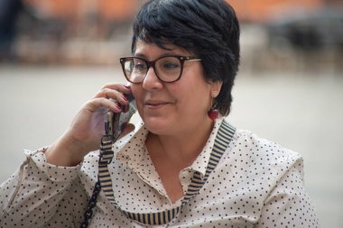 Gözlüklü bir kadın kafede oturmuş telefonla konuşuyor. Modern teknolojiler ve 5G iletişim cihazları kullanılarak