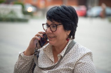 Gözlüklü bir kadın kafede oturmuş telefonla konuşuyor. Modern teknolojiler ve 5G iletişim cihazları kullanılarak