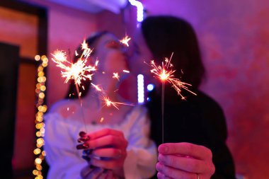 Couple holding sparklers with glowing lights in festive setting at party, selective focus. clipart