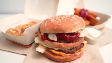 Hamburgerli duble köfte, marul, ketçap, turşu ve peynirli susamlı çörek peçetede fast food ambalajının arka planında..