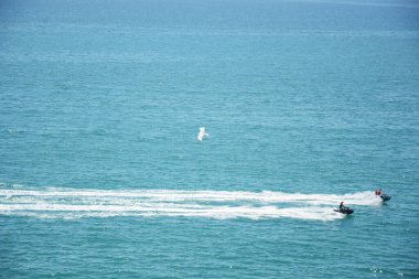 İnsanlar okyanusta jet ski sürüyor, beyaz köpükle dalgalar yaratıyorlar. Su taşımacılığı, yaz eğlencesi, su sporları