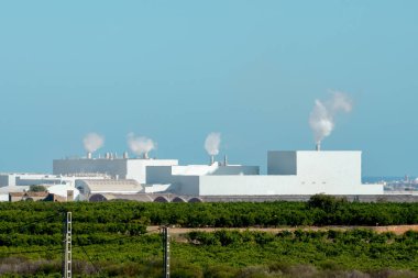 Industrial plant with smokestacks surrounded by green vegetation. Impact of industry and environmental pollution clipart